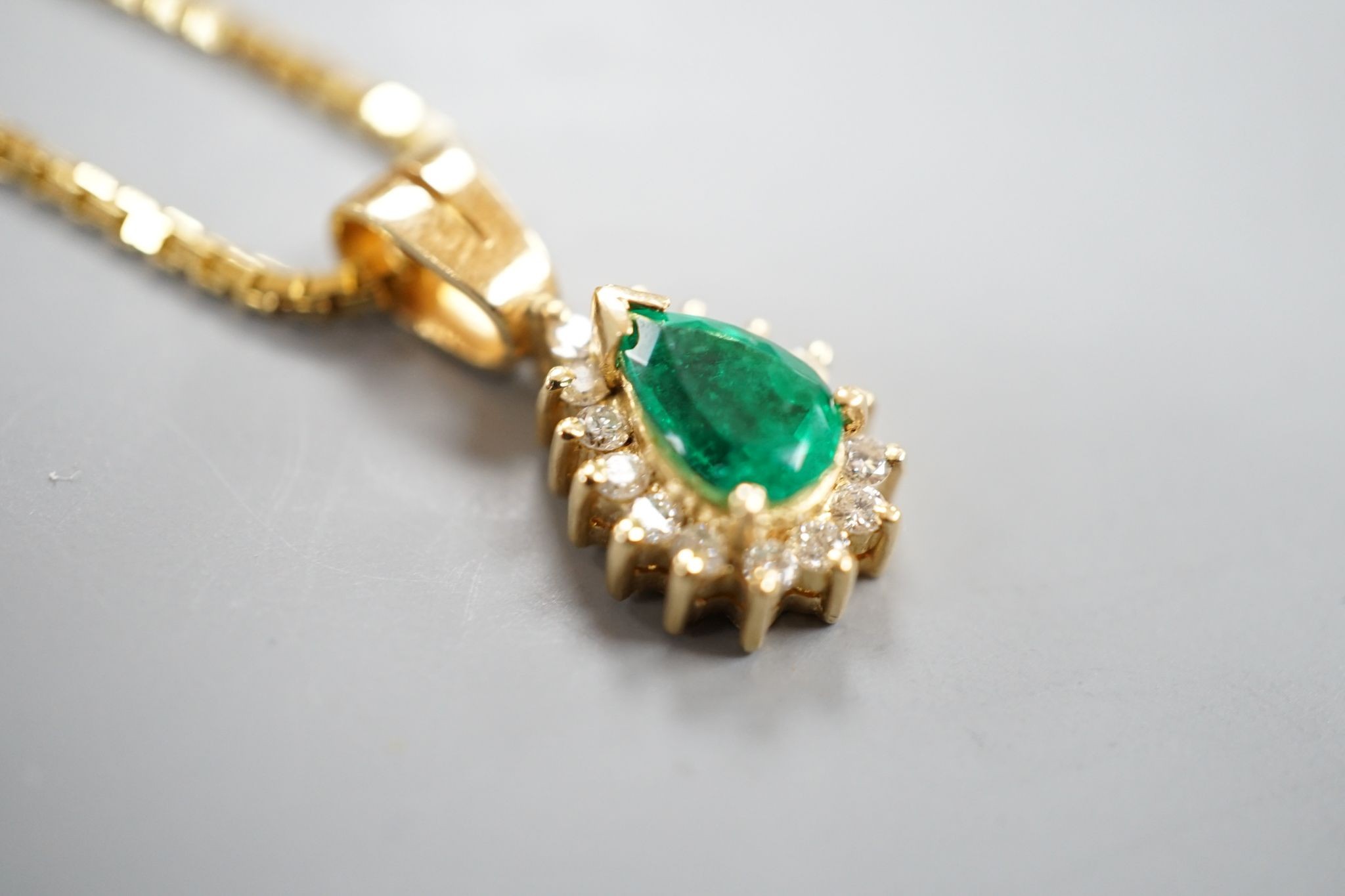 A modern 18k, emerald and diamond cluster set pear shaped pendant, overall 21mm, on an 18k chain, 43cm